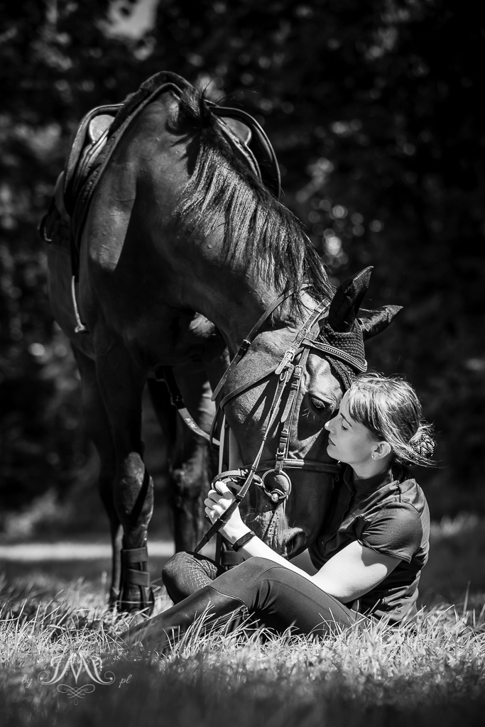 siedząca na trawie kobieta przytulająca konia