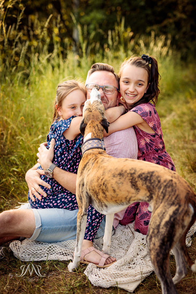 sesja rodzinna - tako z córkami i psem siedzący na trawie
